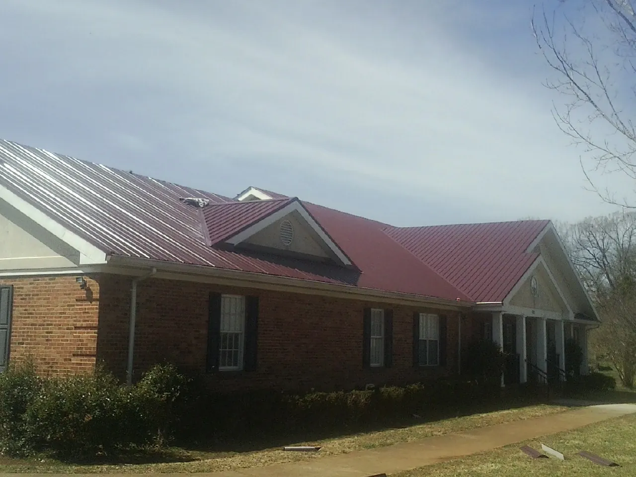 Red metal roof with gabled entries on a long brick building, from a Hail Damage Roof Repair job in Captiva