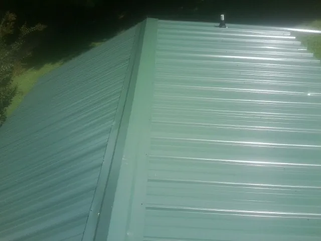New green metal panels meeting at the ridge of a roof — Flat Roof Repair work by our crew in Captiva