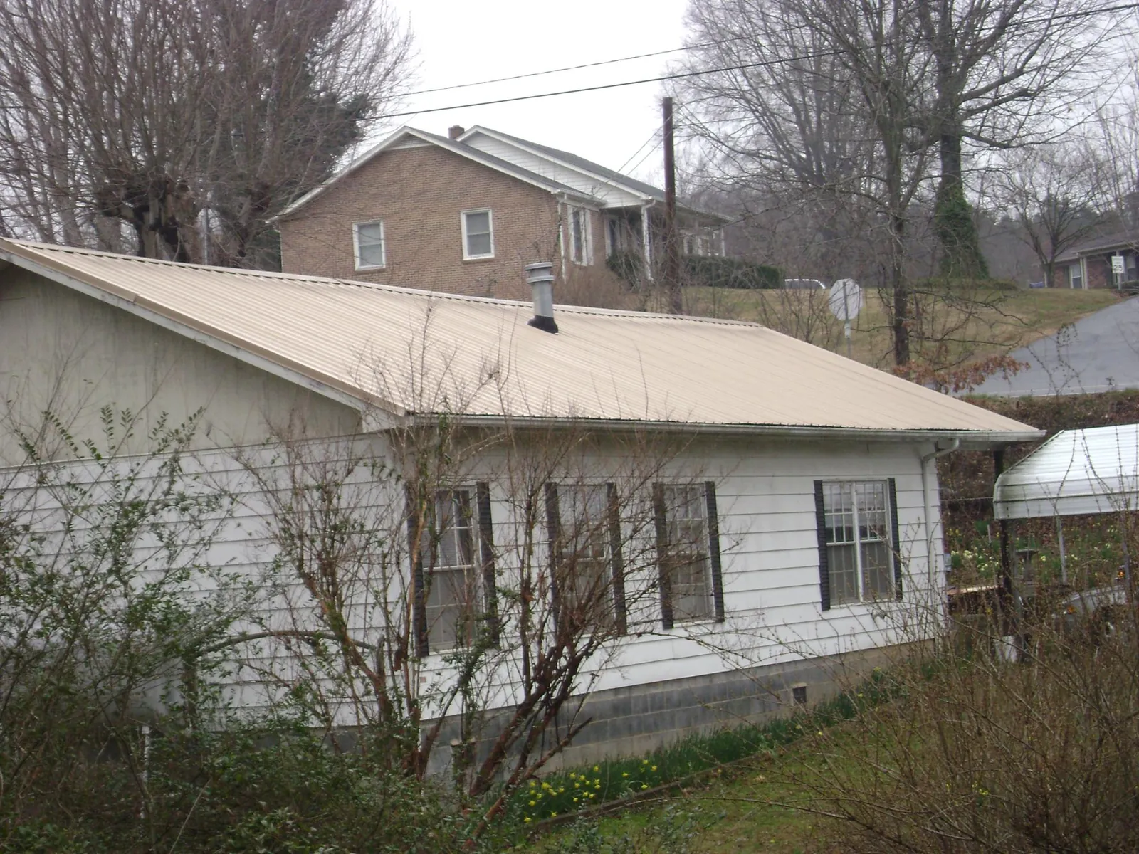 Tan metal roof on a white sided house set into a hillside — Commercial Roofing by Roofing Brothers in Captiva